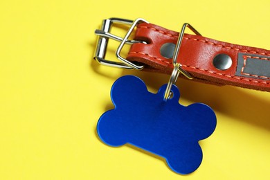 Leather dog collar with blue tag in shape of bone on yellow background, closeup. Space for text