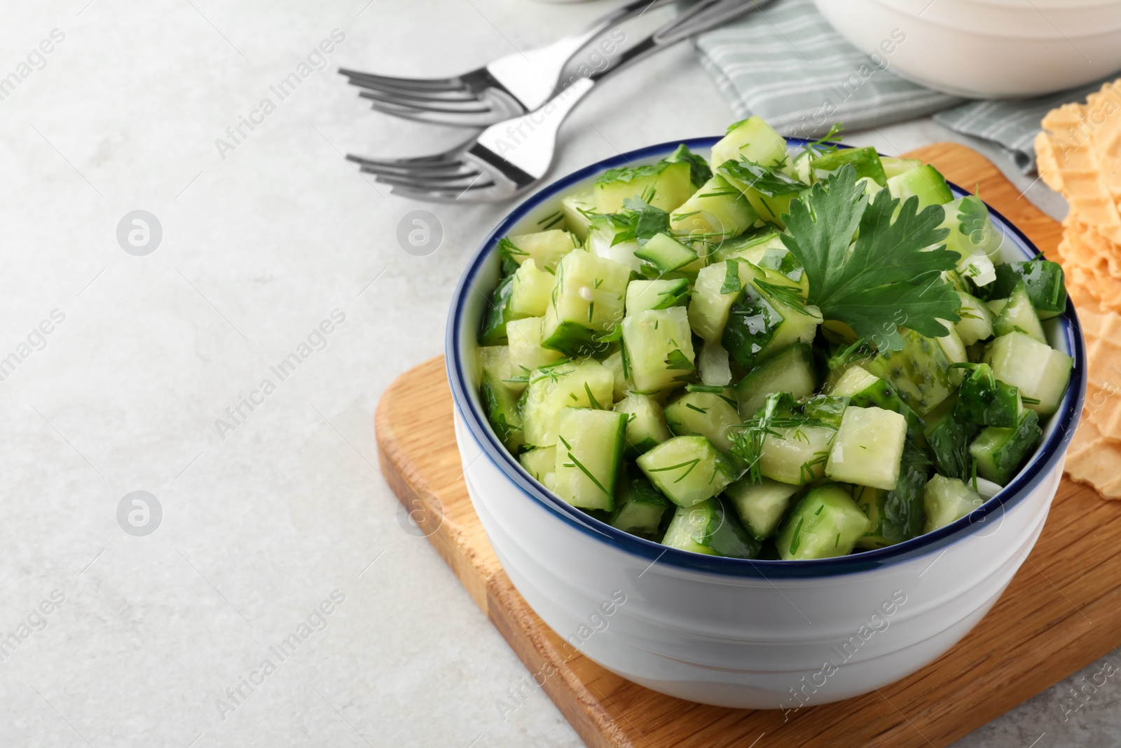 Photo of Bowl of delicious cucumber salad served on light table, closeup. Space for text