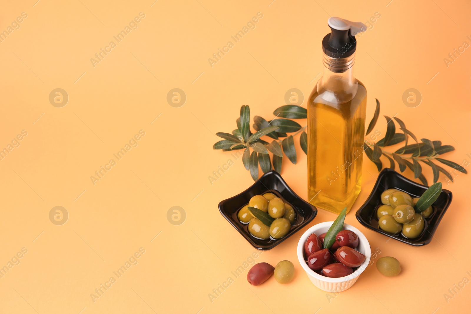 Photo of Bottle of oil, olives and tree twigs on orange background. Space for text