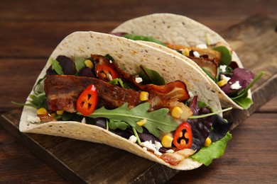 Photo of Delicious tacos with fried bacon, vegetables and cheese on wooden table, closeup