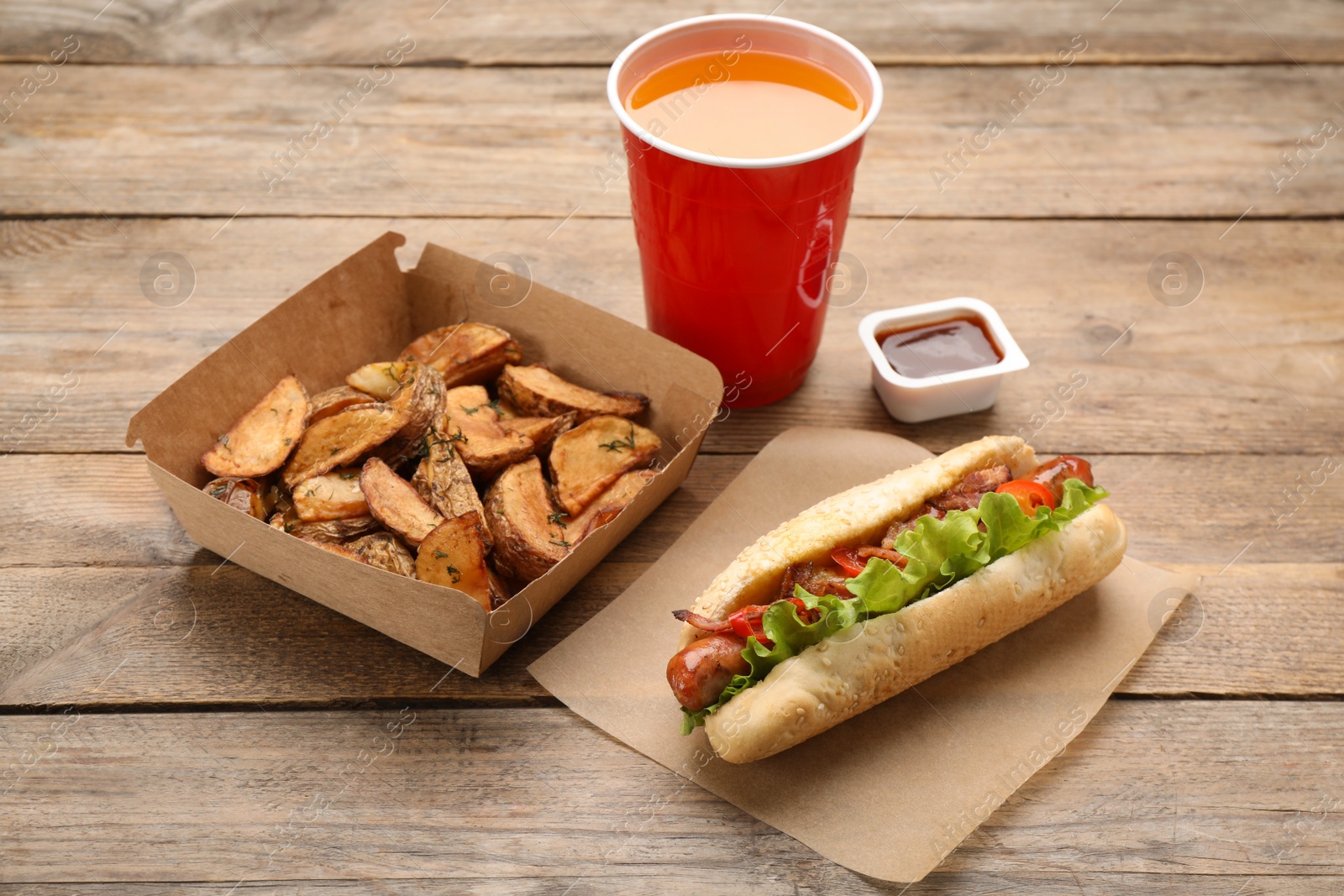 Photo of Hot dog, potato wedges, ketchup and refreshing drink on wooden table. Fast food