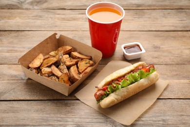 Photo of Hot dog, potato wedges, ketchup and refreshing drink on wooden table. Fast food