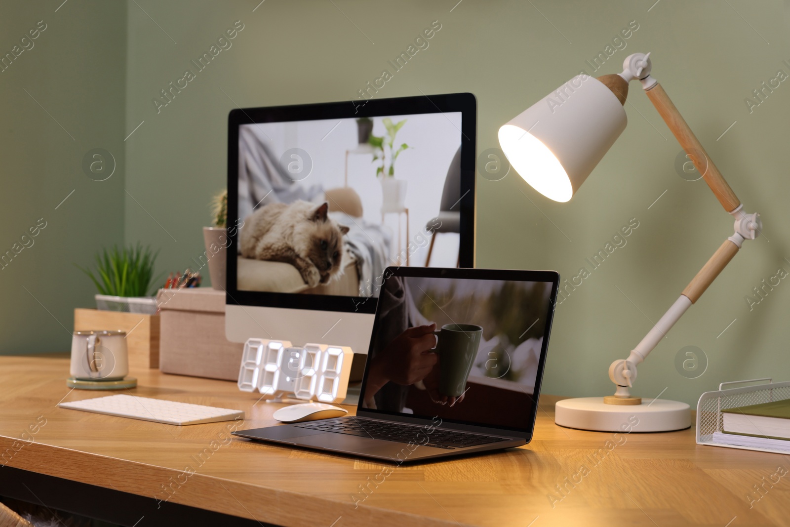 Photo of Stylish workplace with computer, laptop and lamp near olive wall at home