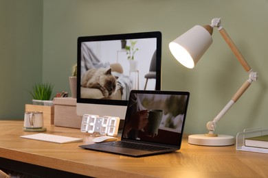 Stylish workplace with computer, laptop and lamp near olive wall at home