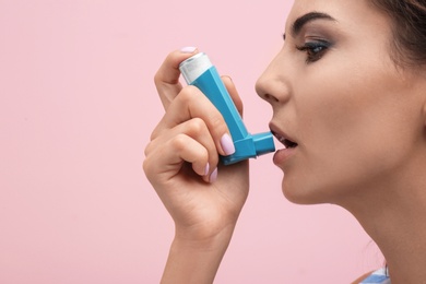 Photo of Young woman using asthma inhaler on color background, closeup