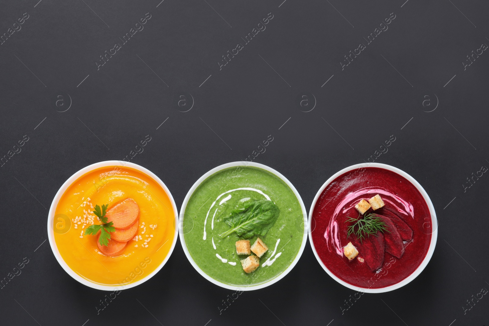 Photo of Various cream soups in bowls and space for text on black background, top view