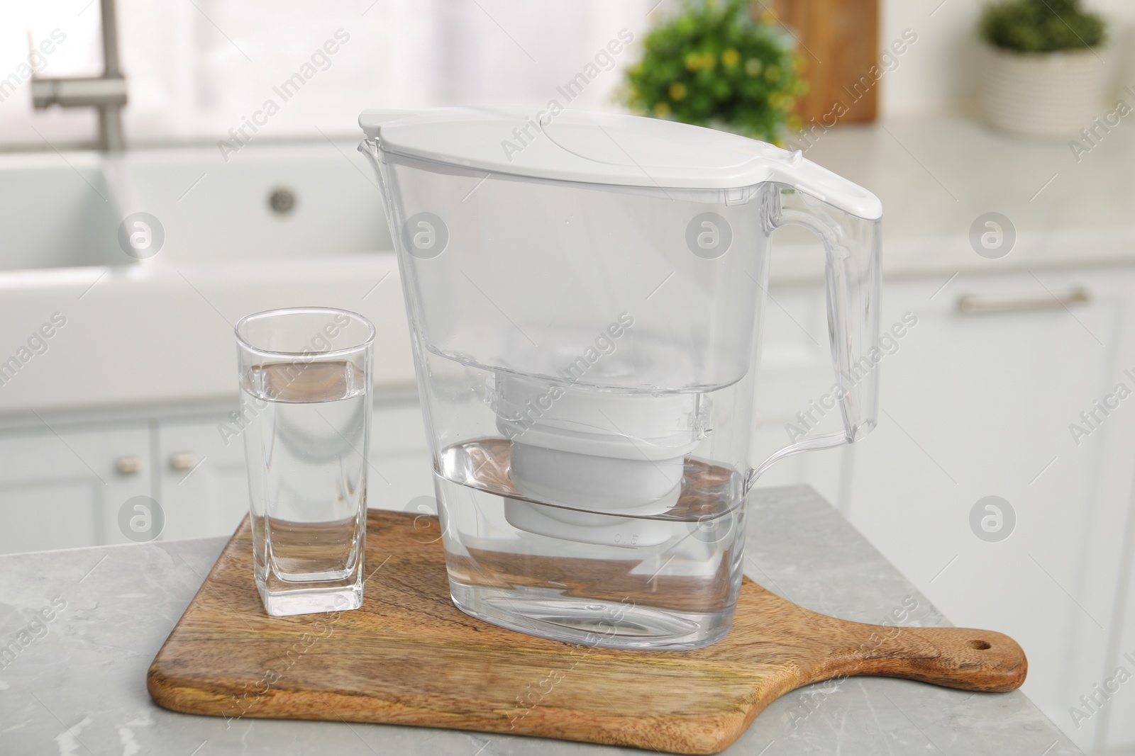 Photo of Water filter jug and glass on light table in kitchen, closeup