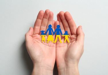 Image of Woman holding paper family figures in colors of Ukrainian flag on light background, top view
