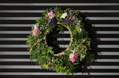 Wreath made of beautiful flowers hanging on grey wall with planks