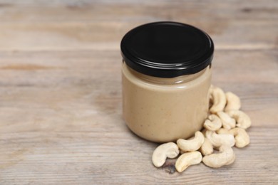 Photo of Tasty nut paste in jar and cashews on wooden table, closeup. Space for text