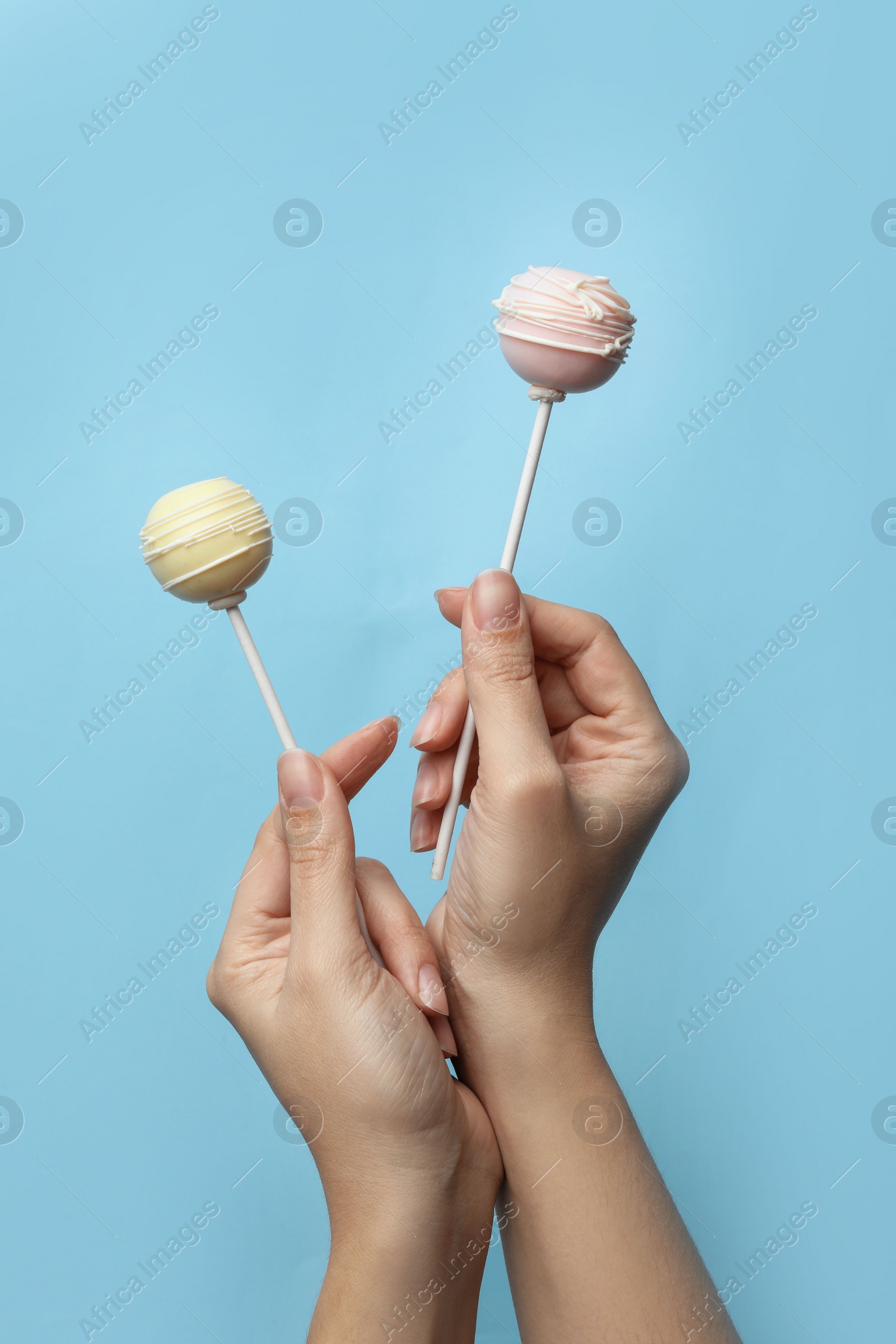 Photo of Woman holding sweet cake pops on light blue background, closeup