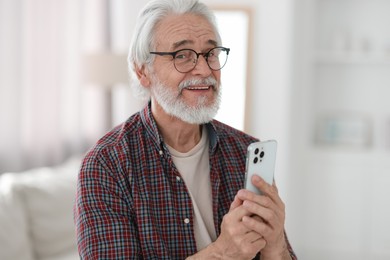 Photo of Portrait of happy grandpa with glasses using smartphone indoors