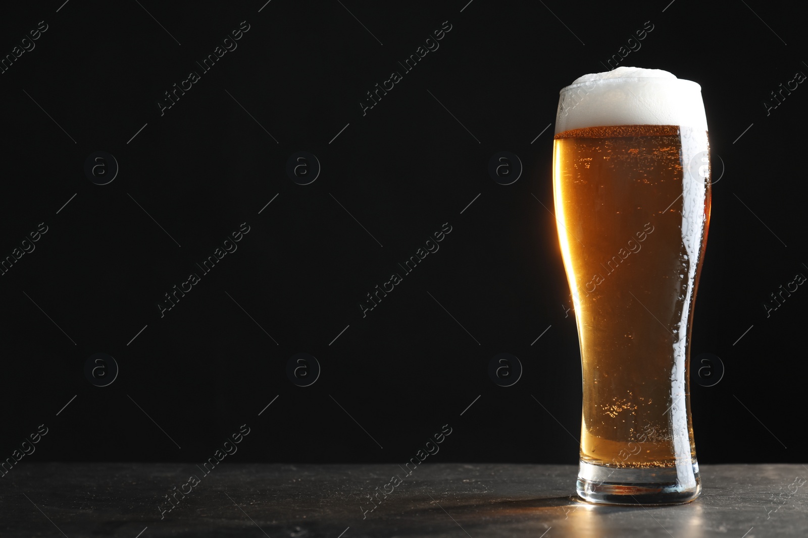 Photo of Cold tasty beer on grey table against dark background. Space for text