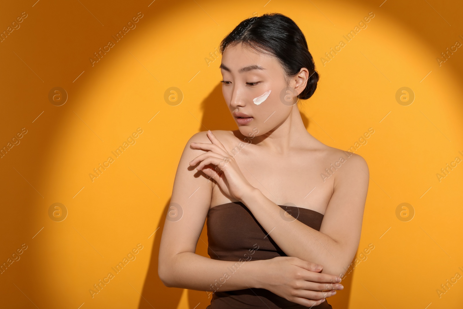 Photo of Beautiful young woman in sunlight with sun protection cream on her face against orange background, space for text