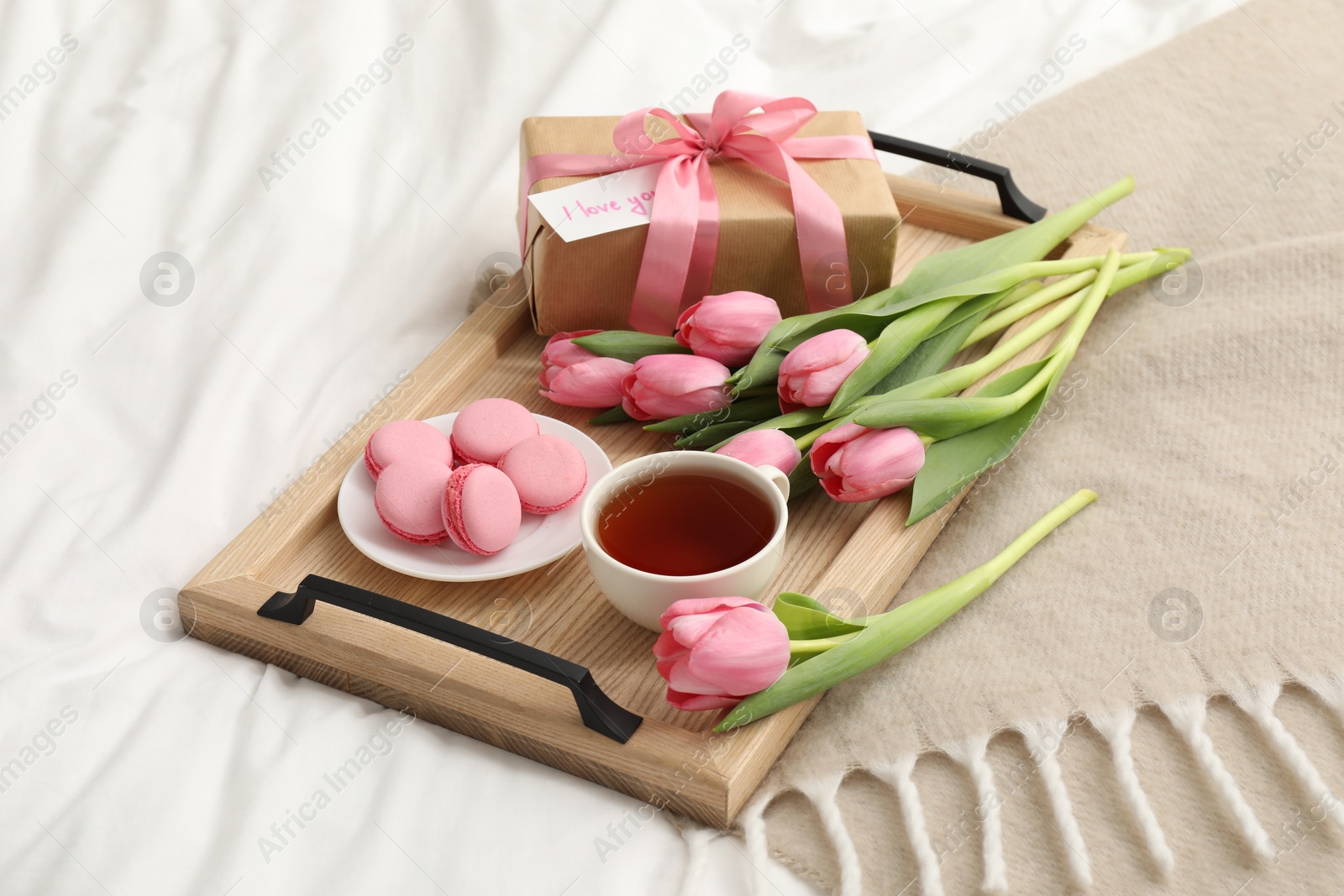 Photo of Tasty breakfast served in bed. Delicious macarons, tea, flowers, gift box and card with phrase I Love You on tray