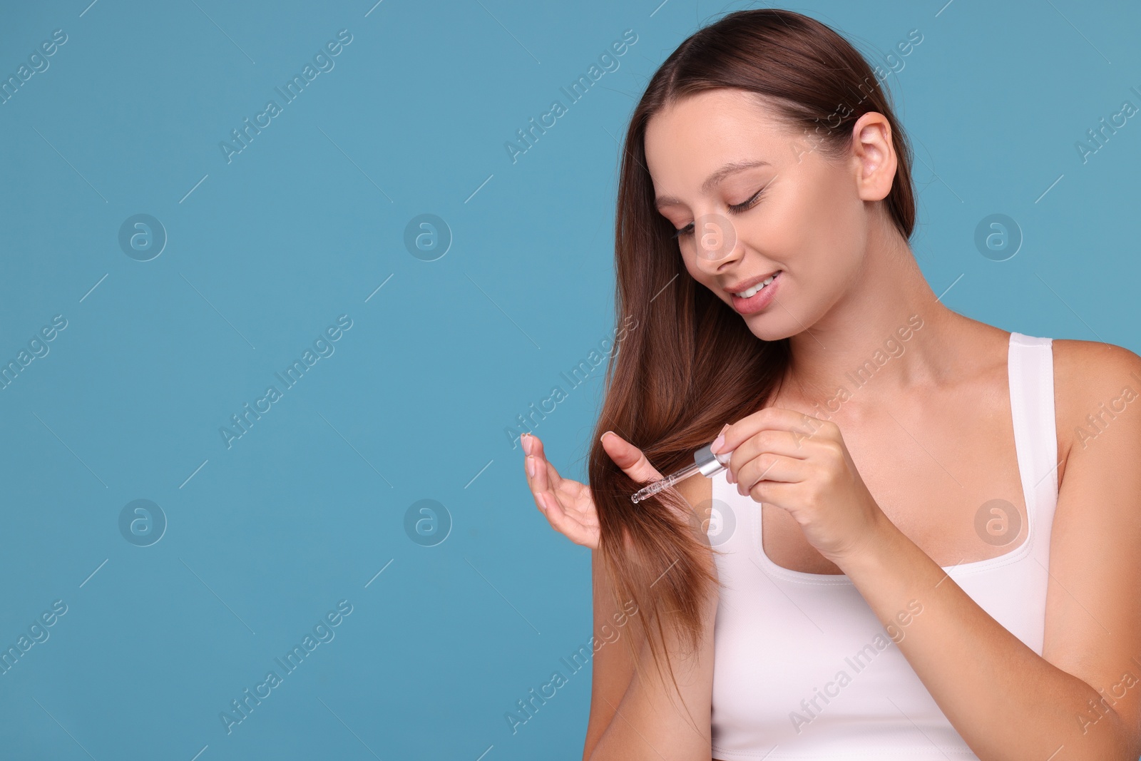 Photo of Beautiful woman applying serum onto hair on light blue background, space for text