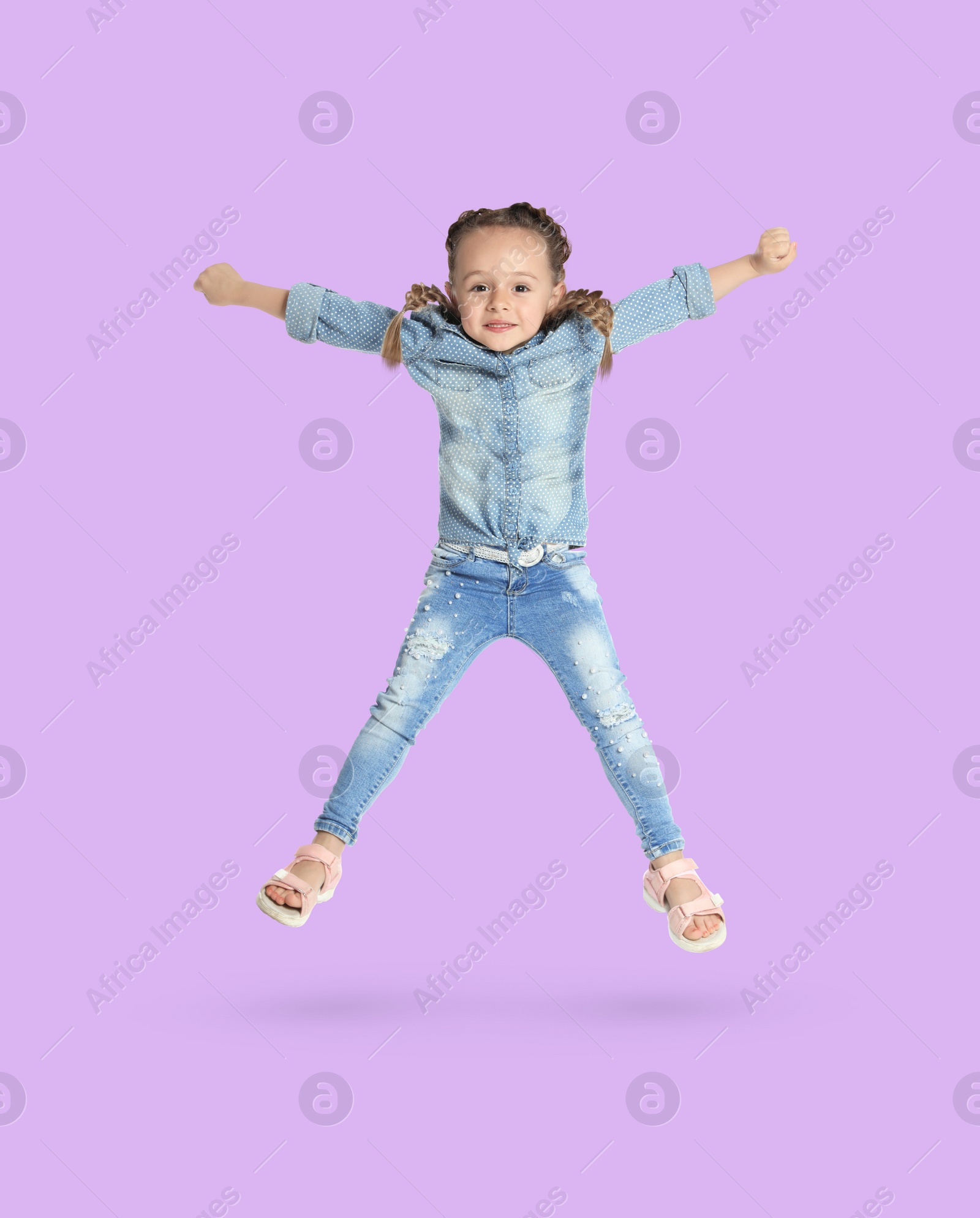 Image of Happy cute girl jumping on light violet background