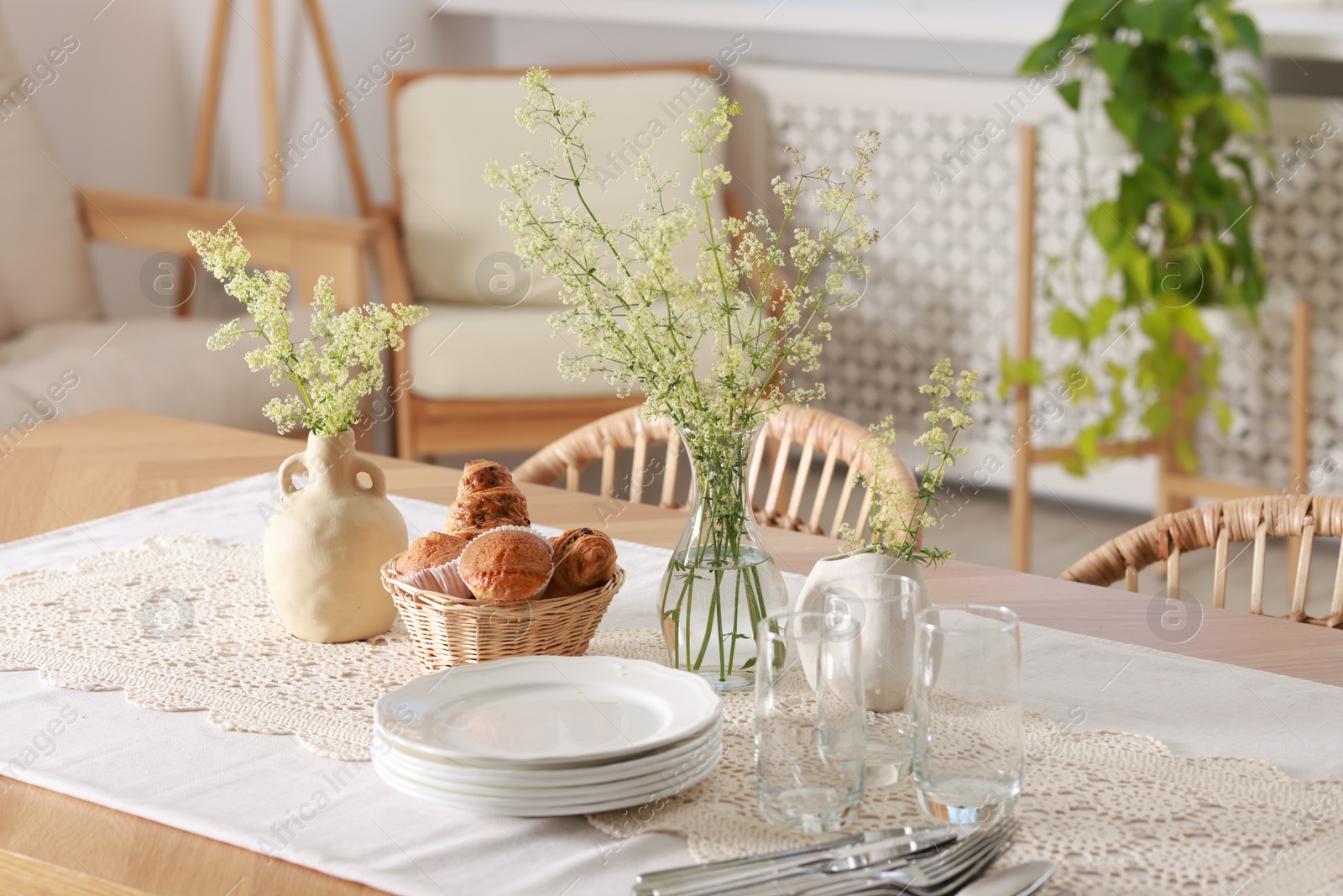 Photo of Clean dishes, flowers and fresh pastries on table in stylish dining room