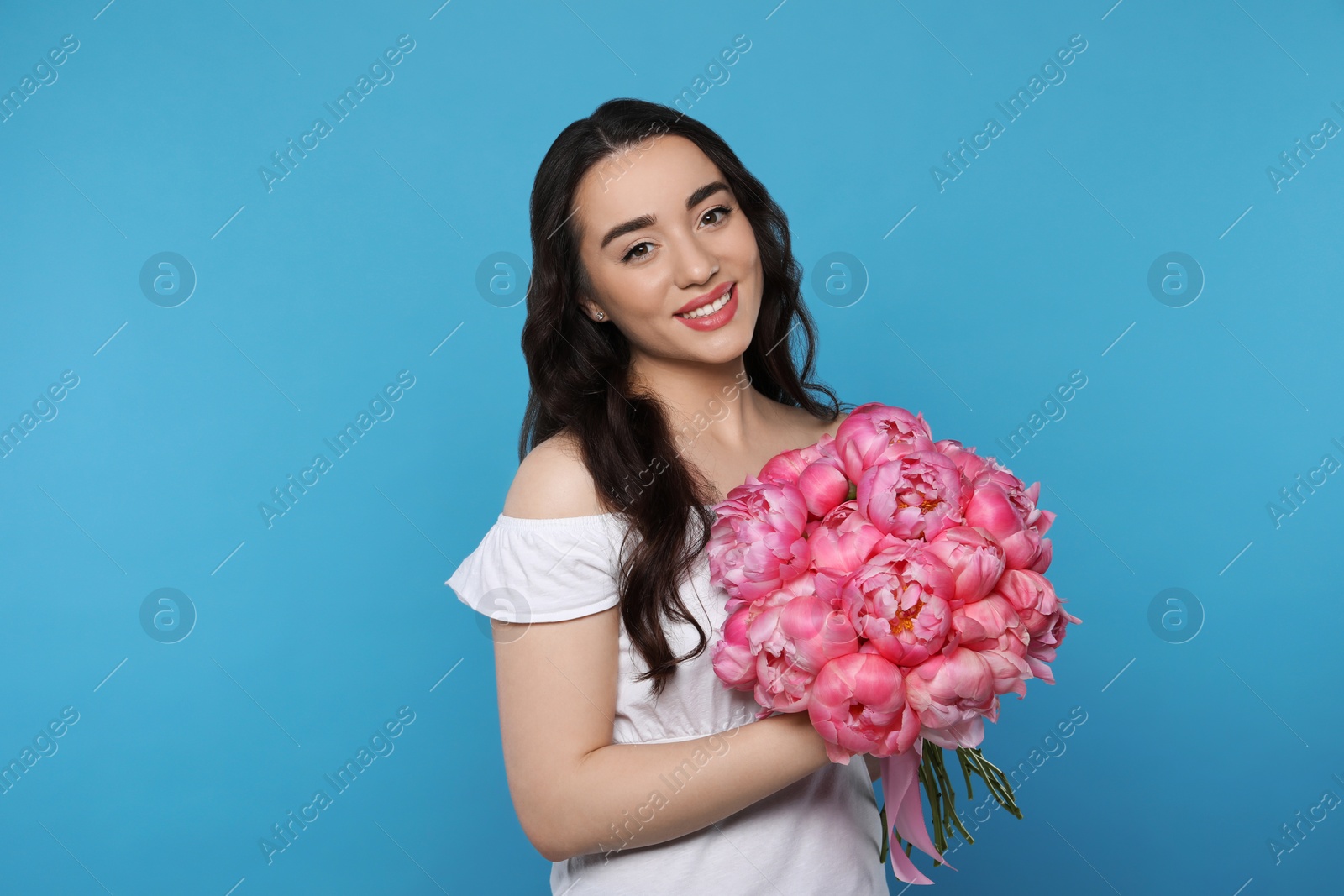 Photo of Beautiful young woman with bouquet of pink peonies on light blue background