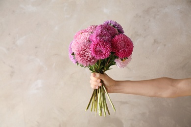 Photo of Woman holding bouquet of beautiful aster flowers on beige background, closeup