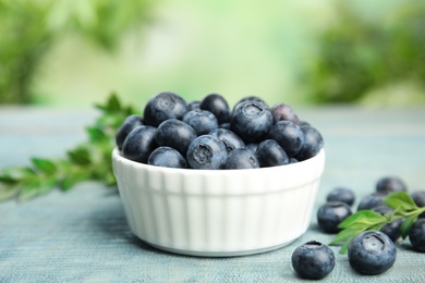 Photo of Bowl of tasty blueberries and leaves on wooden table against blurred green background