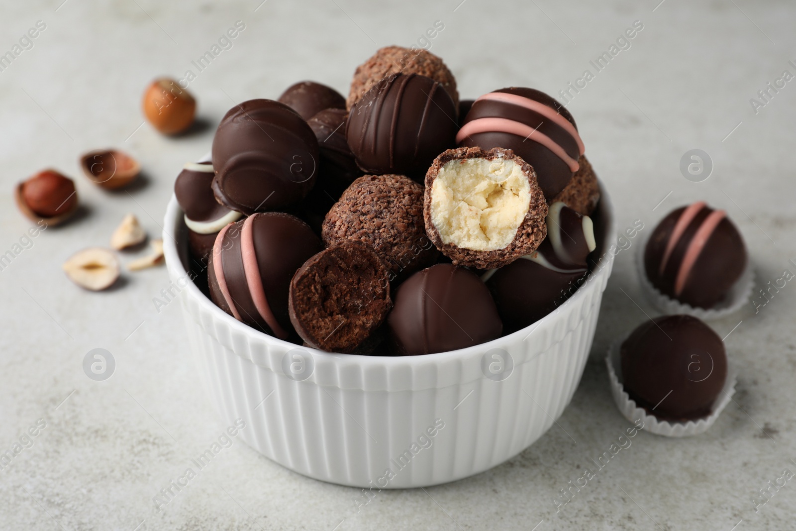 Photo of Different delicious chocolate truffles in bowl on light grey table