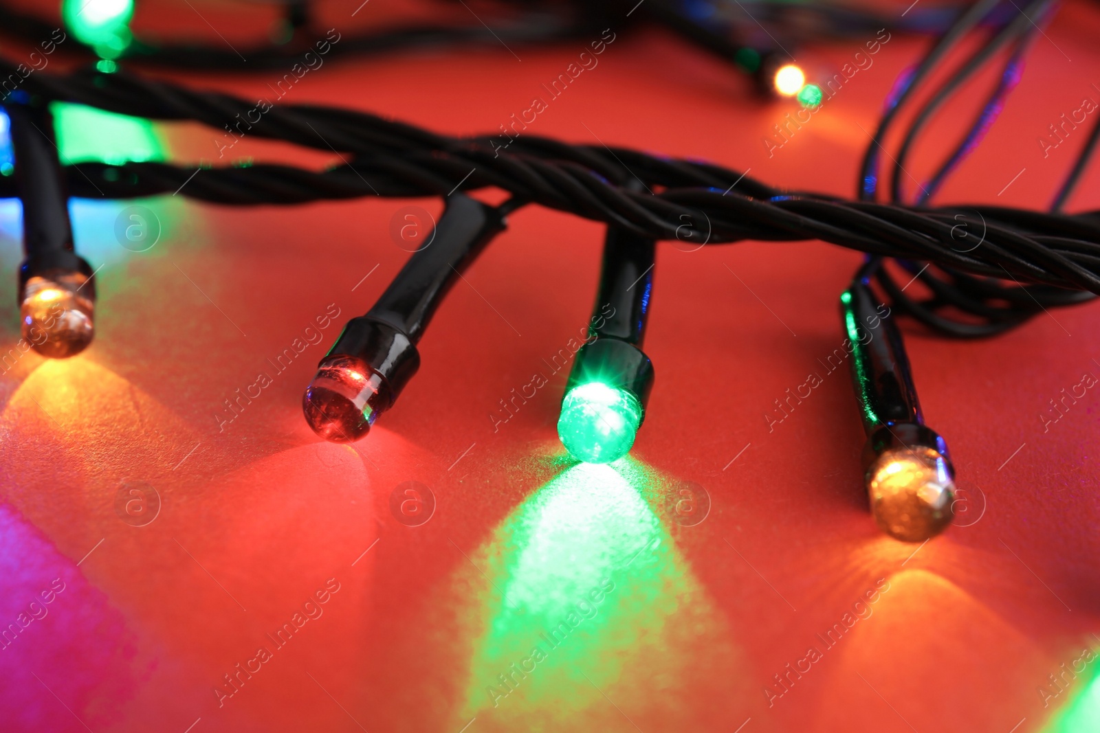 Photo of Glowing Christmas lights on color background, closeup