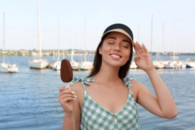 Beautiful young woman holding ice cream glazed in chocolate near river