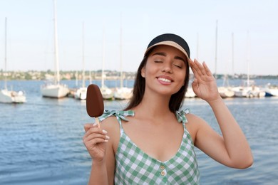 Photo of Beautiful young woman holding ice cream glazed in chocolate near river