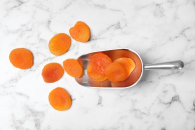 Photo of Scoop with apricots on marble background,  flat lay. Dried fruit as healthy food