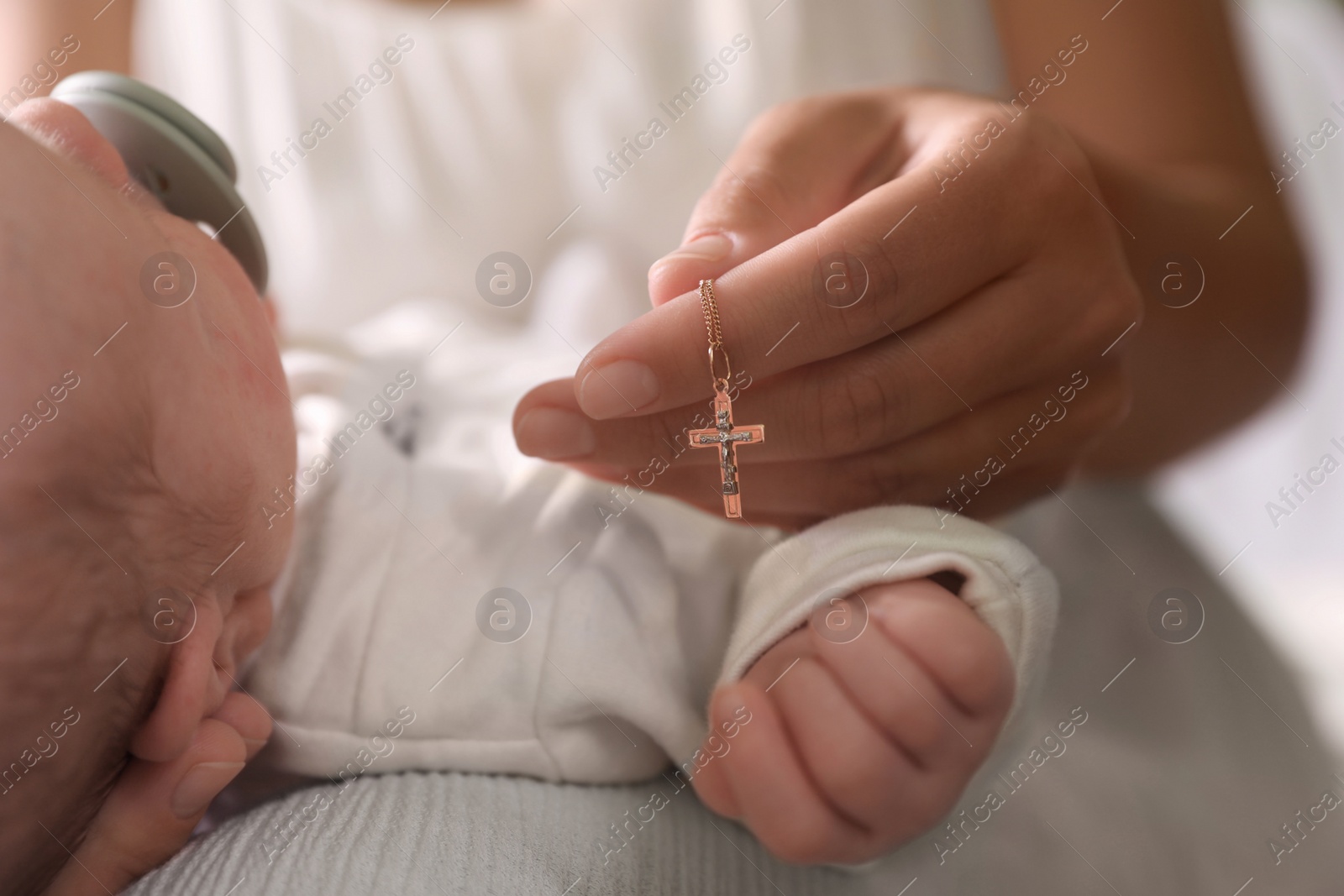 Photo of Mother holding Christian cross near newborn baby indoors, closeup