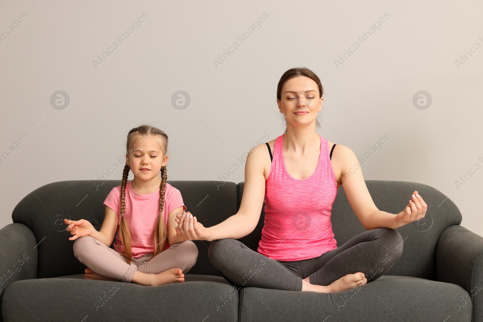 Photo of Mother with daughter meditating on sofa indoors. Harmony and zen