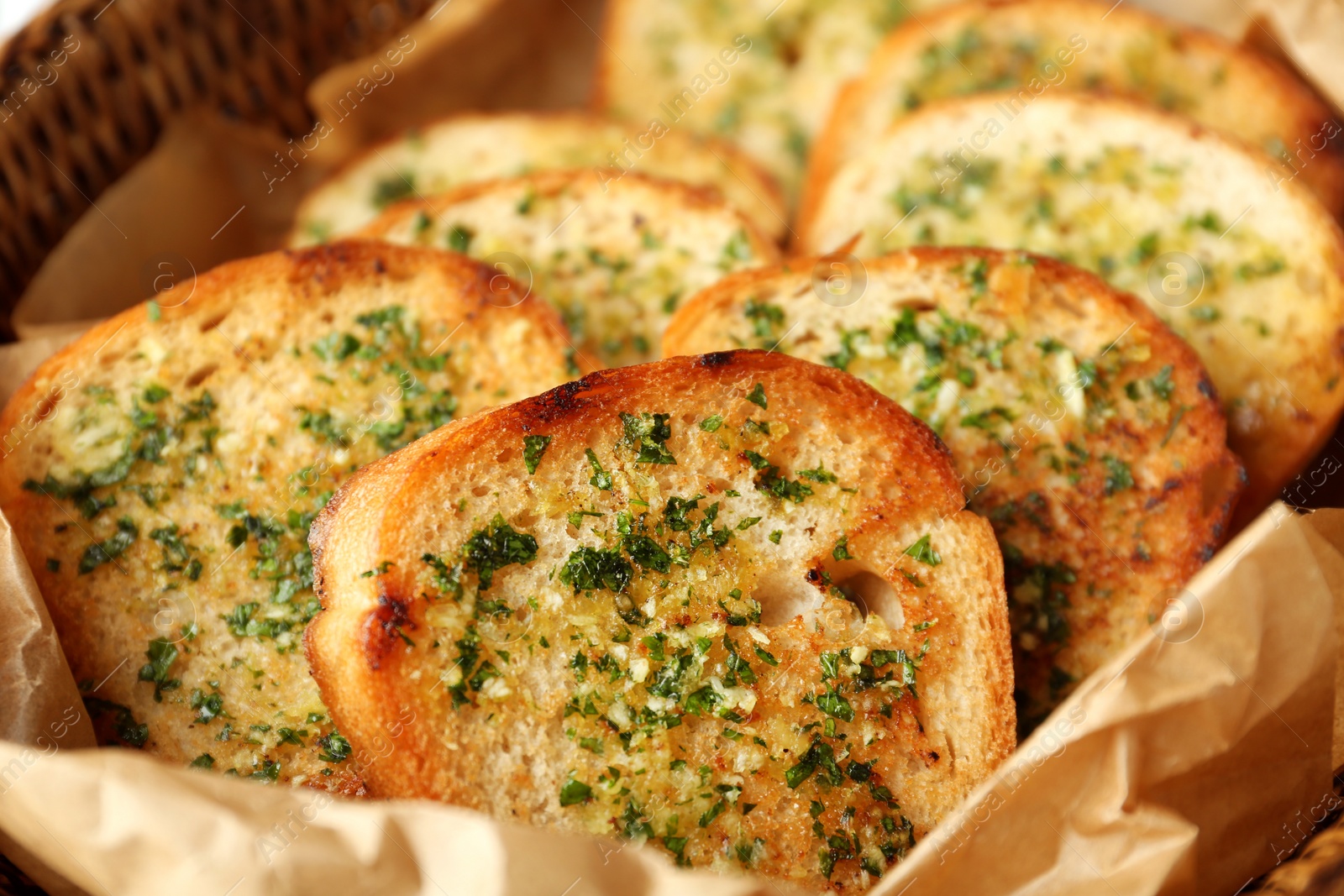 Photo of Slices of toasted bread with garlic and herbs in wicker basket, closeup