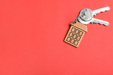 Photo of Keys with trinket in shape of house on red background, top view and space for text. Real estate agent services