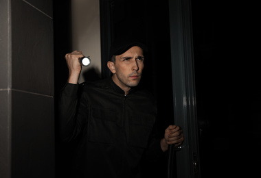 Photo of Male security guard with flashlight near entrance door at night