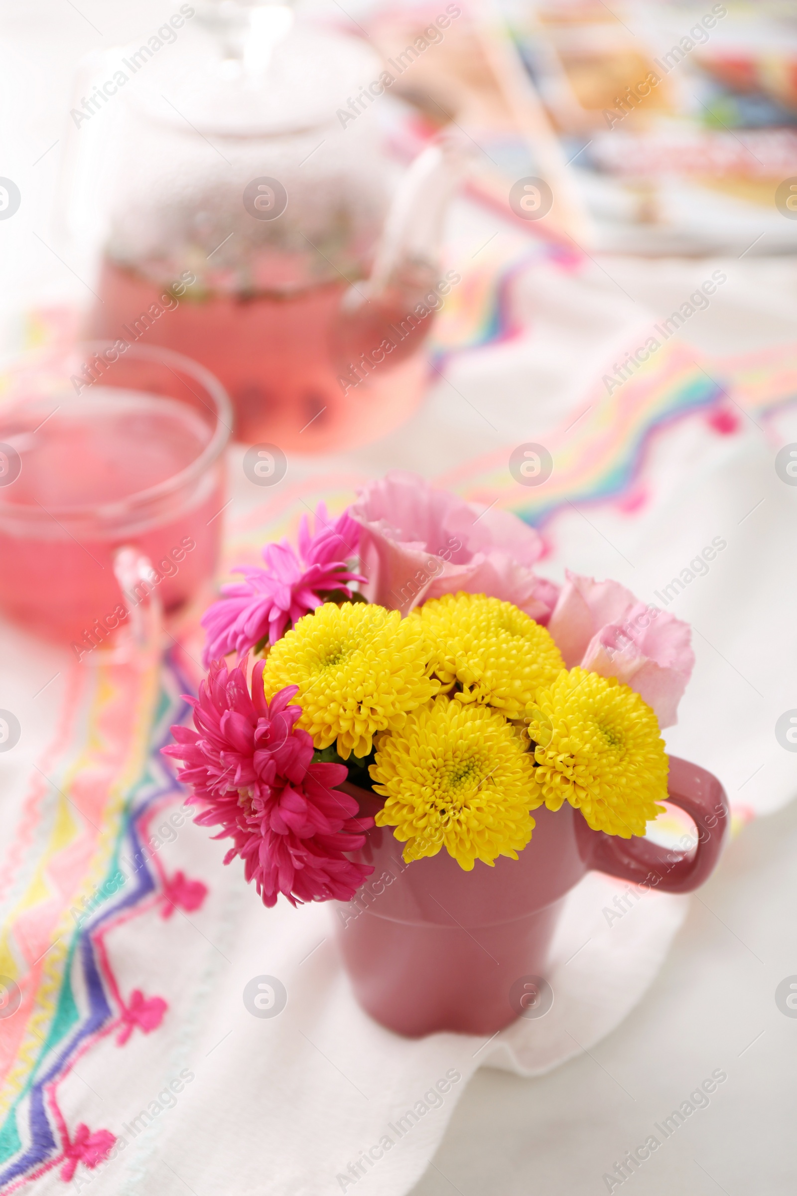 Photo of Beautiful bright flowers in pink cup, fabric and aromatic tea on table