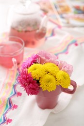 Beautiful bright flowers in pink cup, fabric and aromatic tea on table