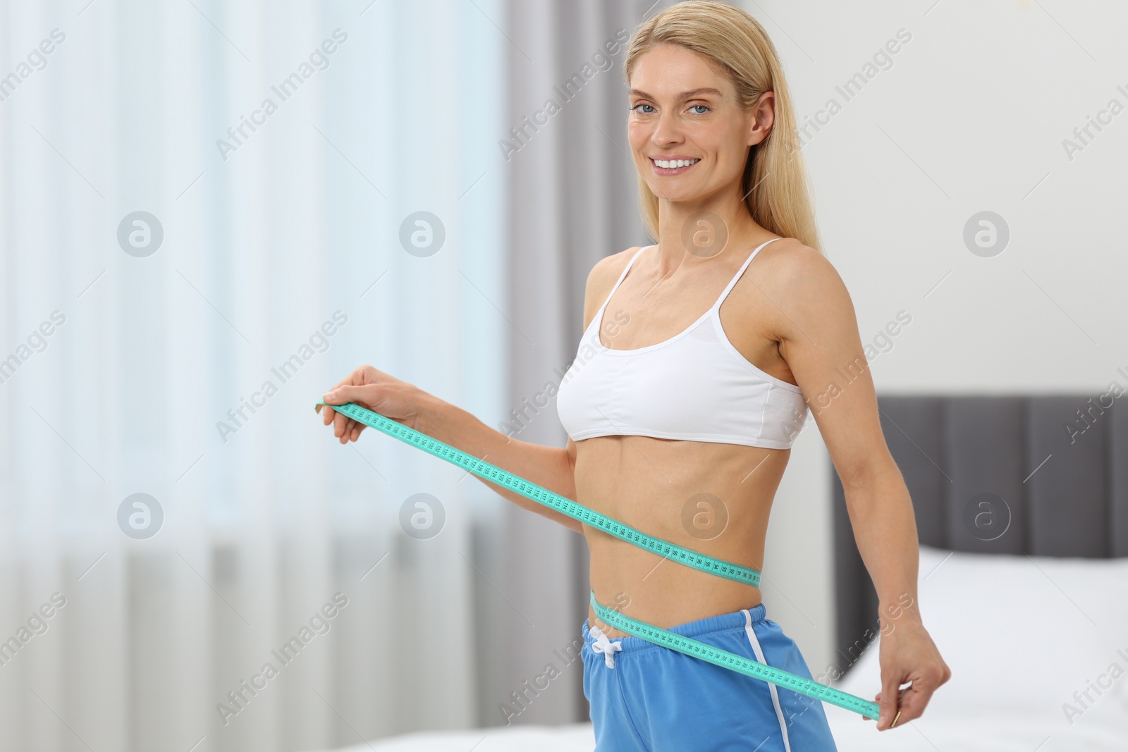 Photo of Slim woman measuring waist with tape at home, space for text. Weight loss