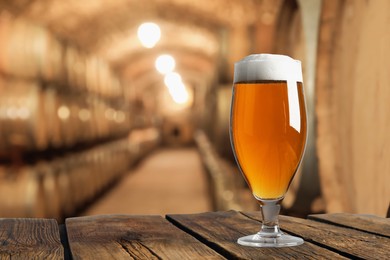 Image of Glass with fresh beer on wooden table in cellar, space for text