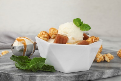 Photo of Bowl of delicious ice cream with caramel candies, popcorn and mint on table