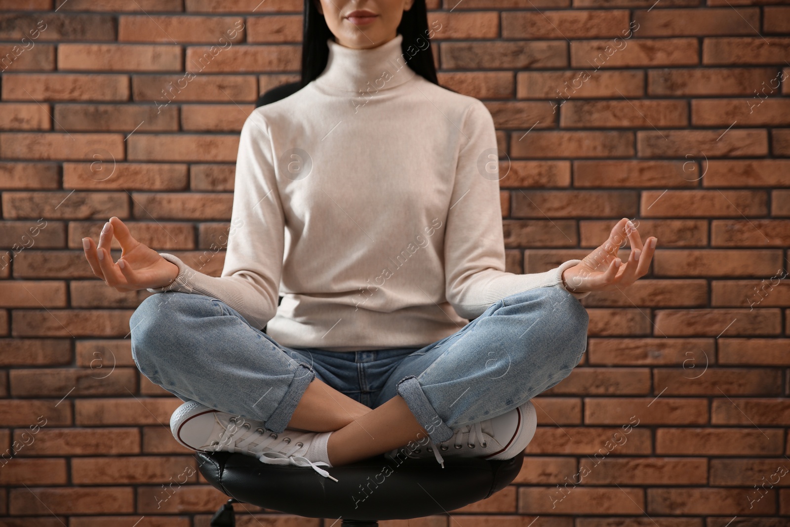 Photo of Woman meditating on chair near brick wall, closeup