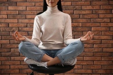 Photo of Woman meditating on chair near brick wall, closeup