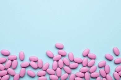 Photo of Many pink dragee candies on light blue background, flat lay. Space for text