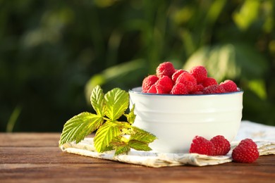 Photo of Tasty ripe raspberries and green leaves on wooden table outdoors, space for text