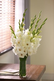 Photo of Vase with beautiful white gladiolus flowers on wooden table in room
