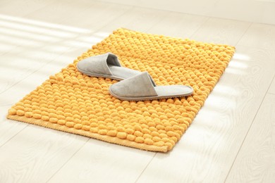 Photo of New yellow bath mat with soft slippers on floor