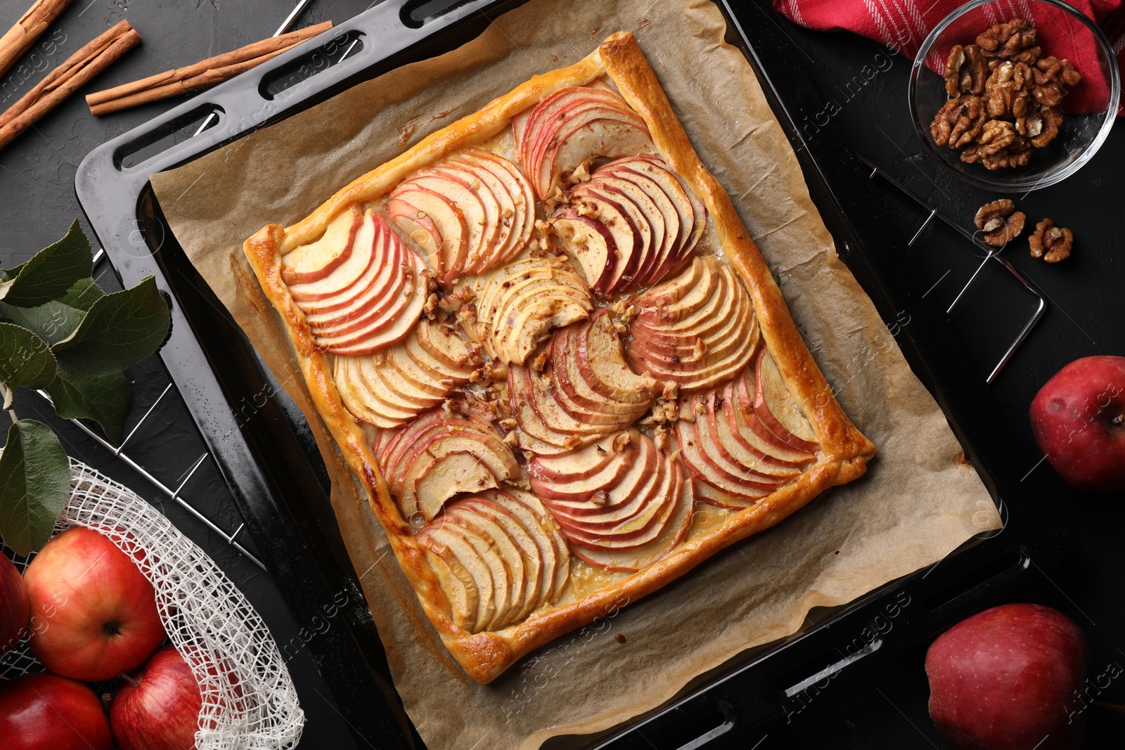 Photo of Baking tray with fresh apple galette and ingredients on black table, flat lay
