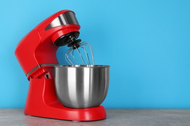 Photo of Modern red stand mixer on gray marble table against turquoise background, space for text