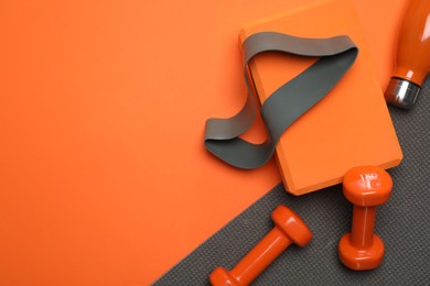 Photo of Dumbbells, yoga block, mat, thermo bottle and fitness elastic band on orange background, flat lay. Space for text