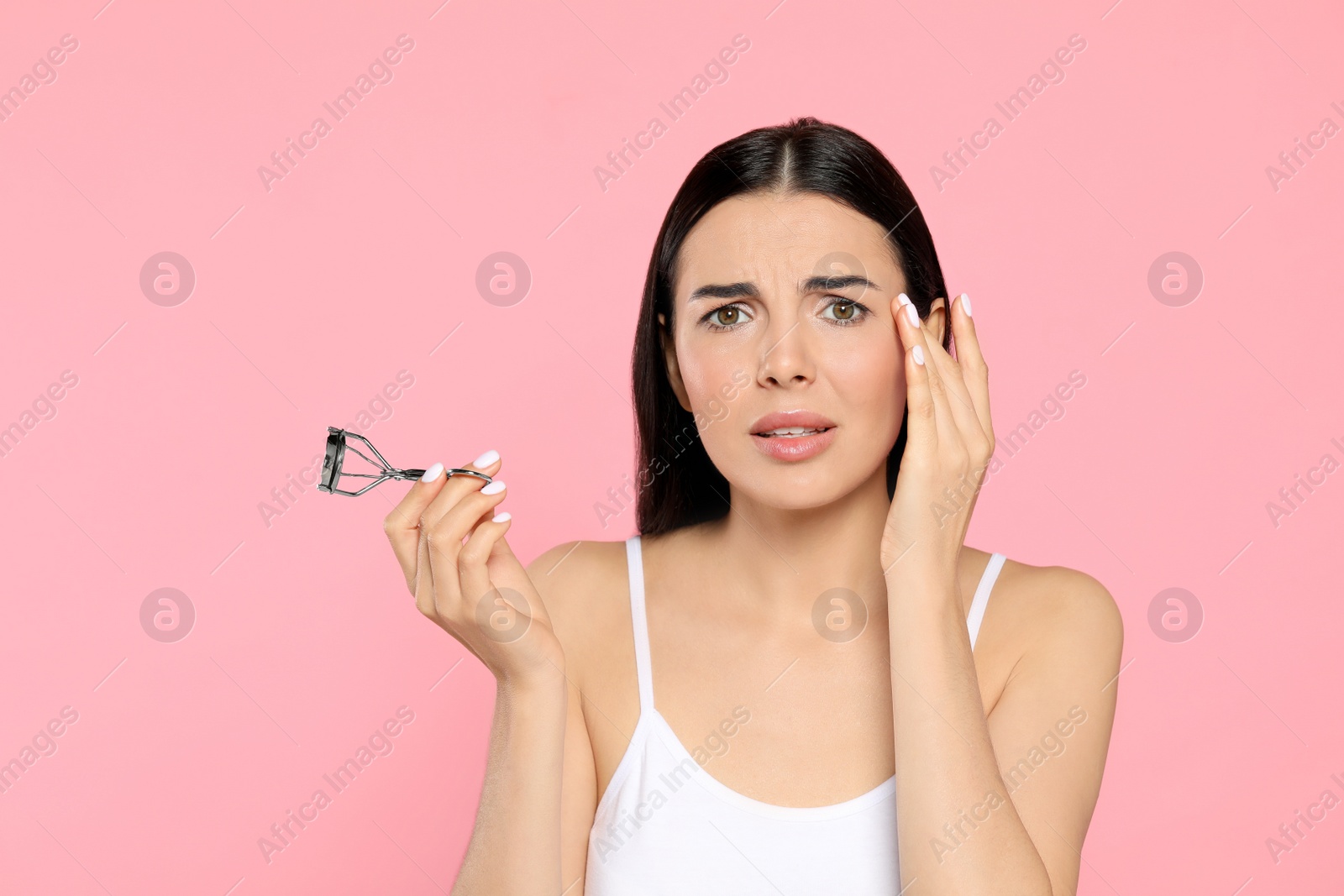 Photo of Emotional young woman with eyelash curler on light pink background